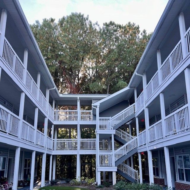 Courtyard view of a gray apartment building with white railings and trees above