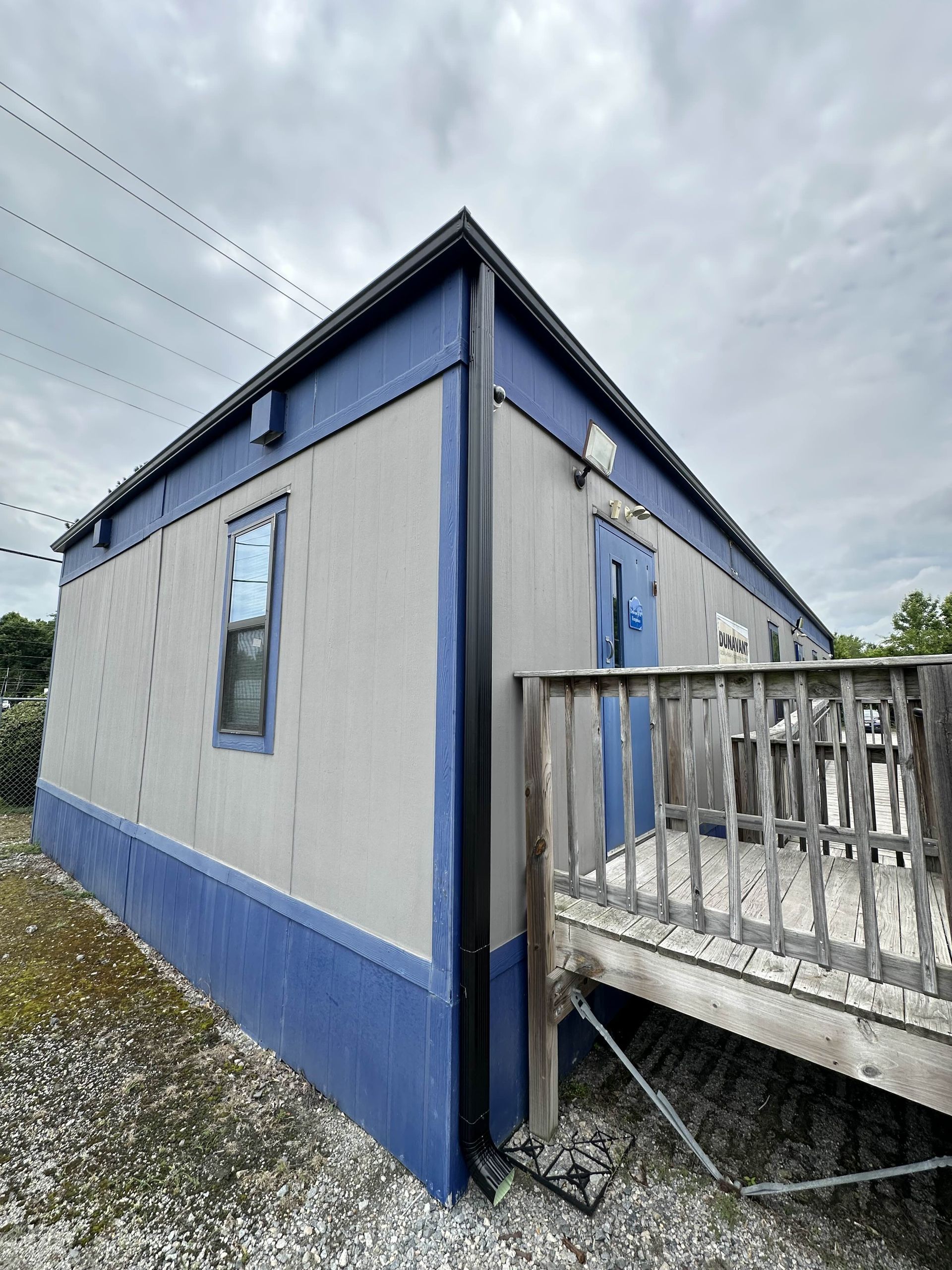 Blue-and-gray mobile home with a wooden porch and cloudy sky overhead