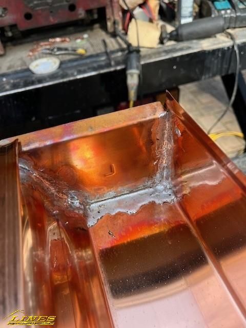 Copper gutter with silver soldering at the corner. Workshop setting.