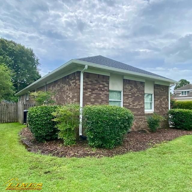 Brick building with white trim, gutters, and windows; surrounded by bushes, mulch, and green grass.