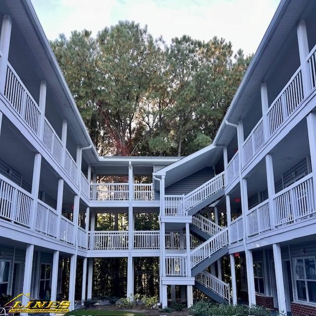 Multi-story apartment building with white railings and staircases, surrounded by trees.