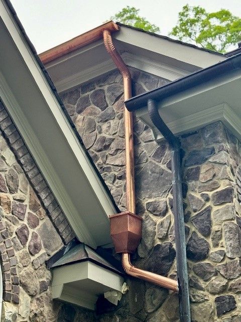Copper gutters and downspouts on a stone house, against a pale green roof.