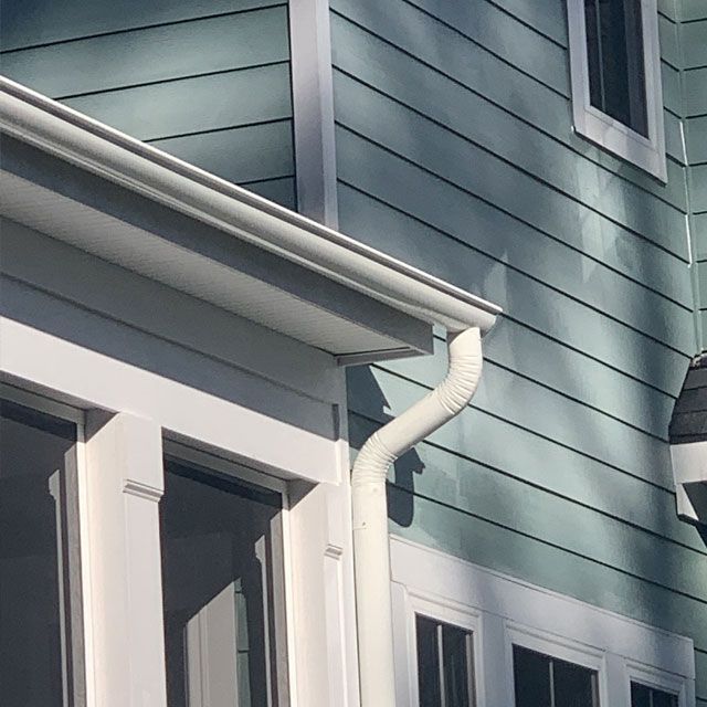 White gutter and downspout on a light blue house with white trim and windows.