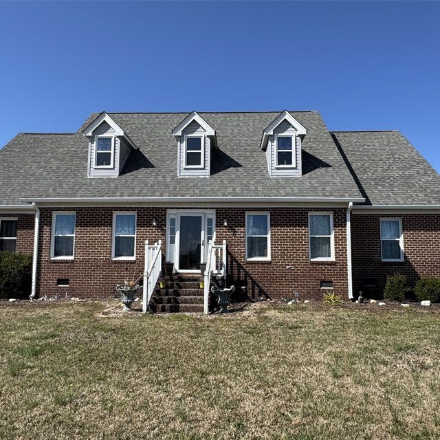 Brick house with gray roof, three dormers, white trim, and steps leading to the front door.