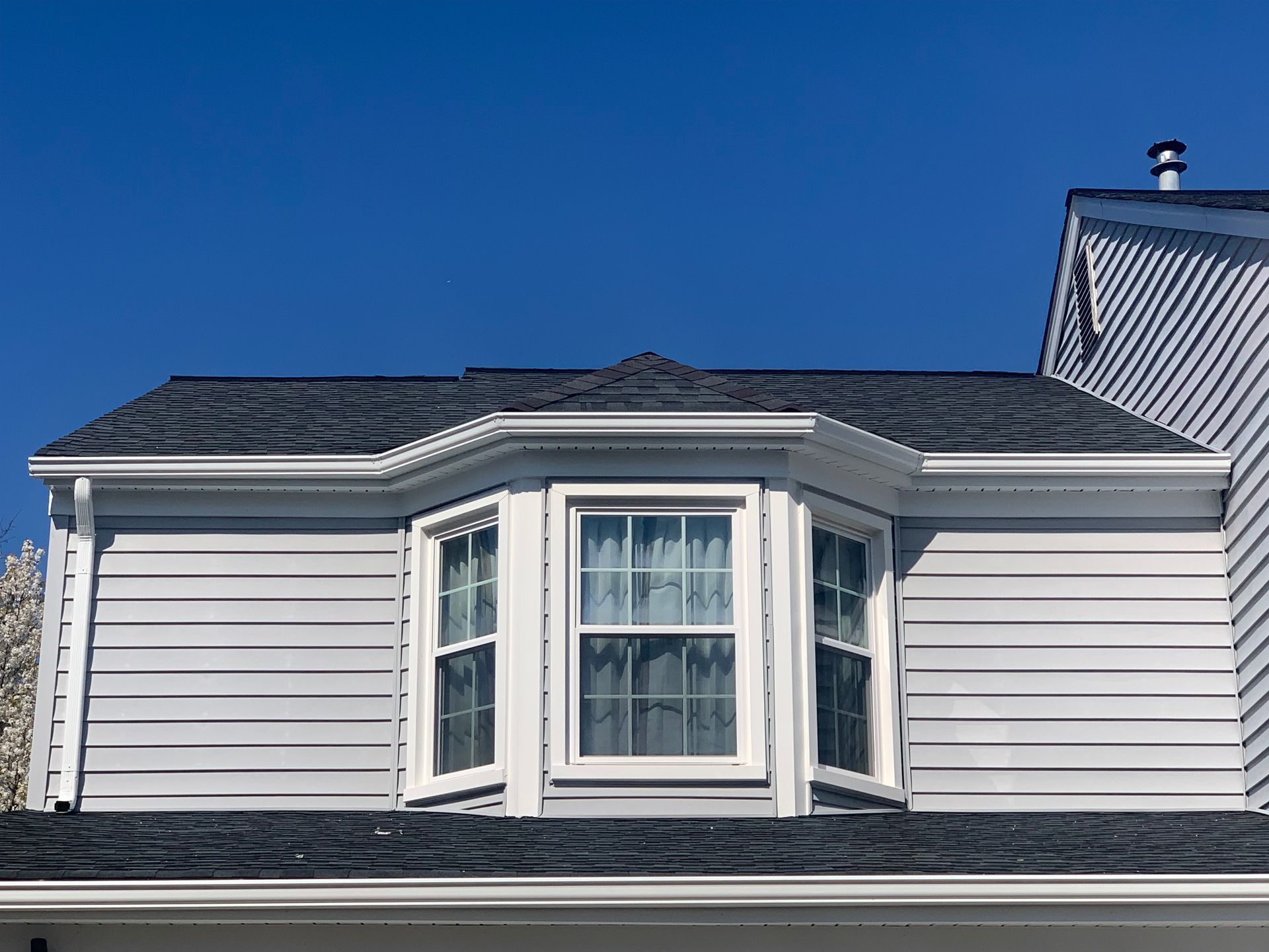 Gray house with a bay window under a dark gray roof against a clear blue sky.