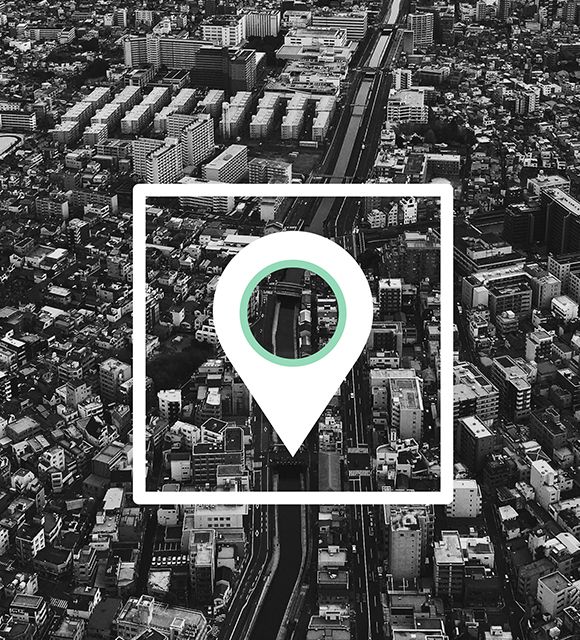 Black-and-white aerial cityscape with a location pin icon centered over a road.