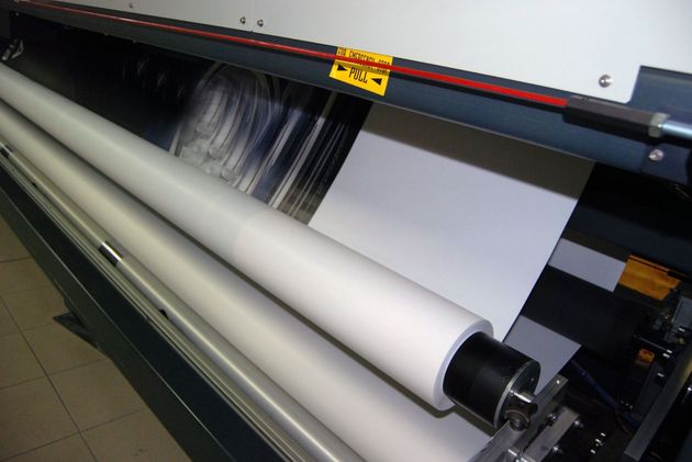 Large-format printer feeding a white sheet through rollers, printing a dark image on glossy paper