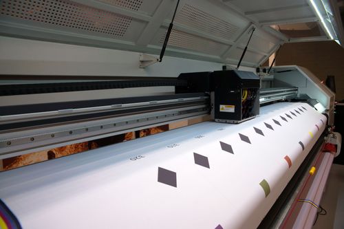 Industrial printer producing a long white roll of paper with colored squares in a workshop