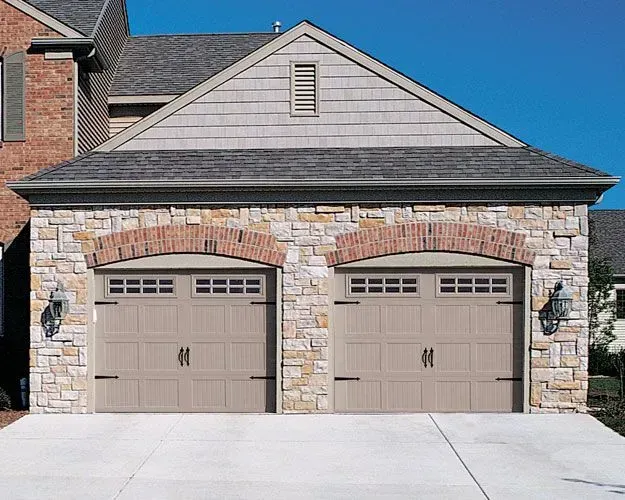 Tan garage doors with brick archways and stone facade under a gabled roof.