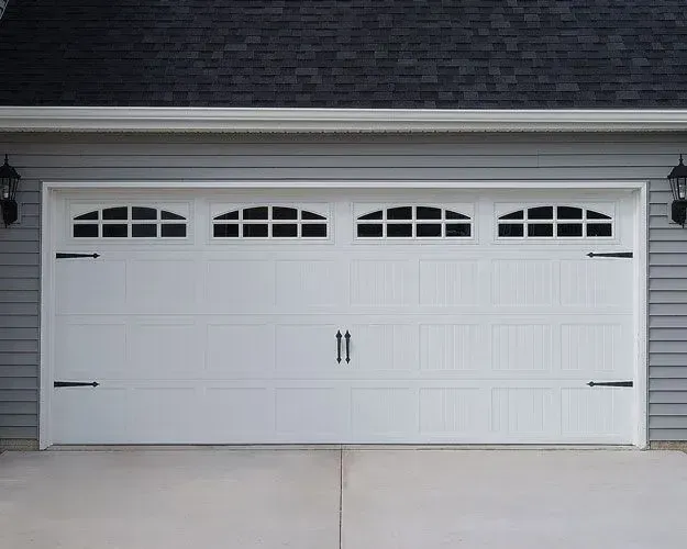 A white garage door with black handles is on the side of a house.