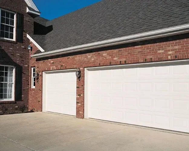 There are two white garage doors on the side of a brick house.