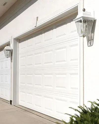 Two white garage doors with lanterns on the side of a house.