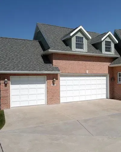 A brick house with two white garage doors and a gray roof