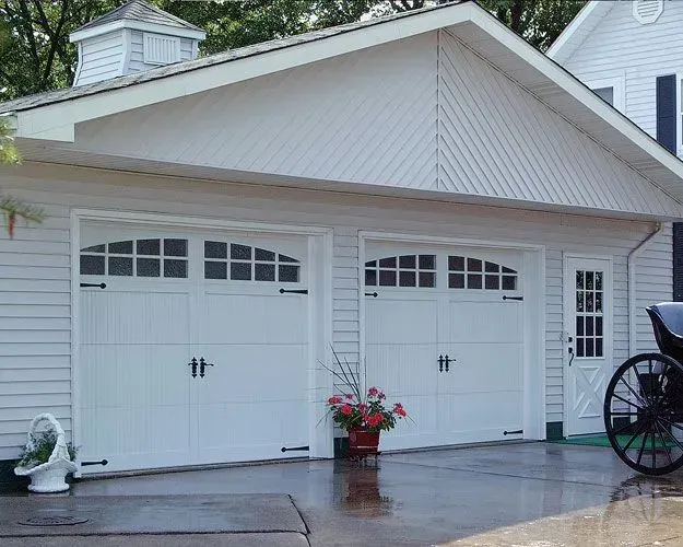 A horse drawn carriage is parked in front of a white garage door.