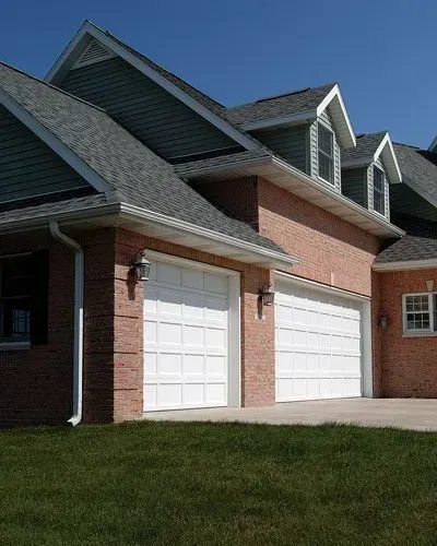 A brick house with two white garage doors and a gray roof