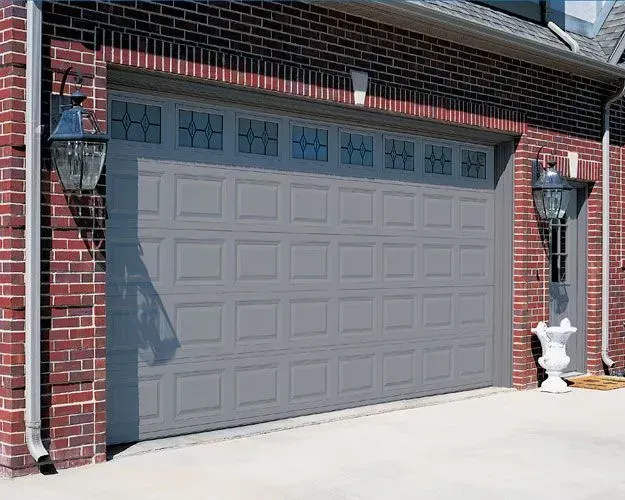 A gray garage door is sitting in front of a brick house.
