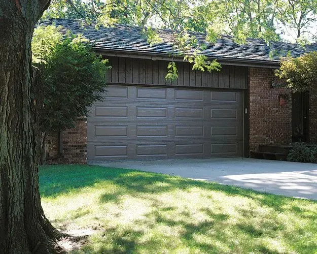 A brown garage door is sitting in front of a brick house.