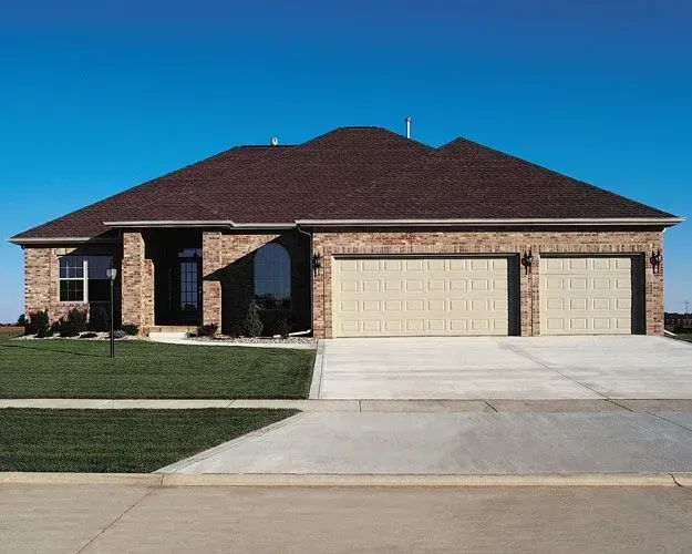 A brick house with two garage doors and a concrete driveway