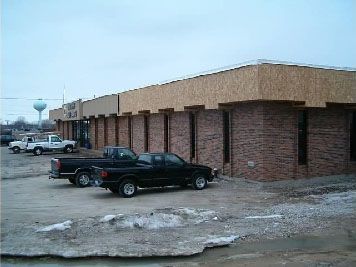 A one-story brick commercial building under renovation with plywood panels on the roofline and trucks parked in the lot.