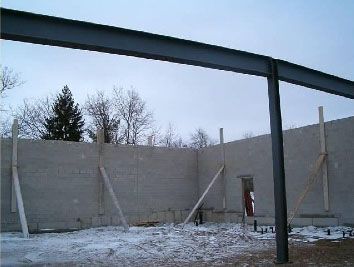 Construction site with concrete walls braced by wooden supports and a large metal support beam against a winter sky.