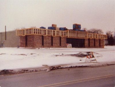 A one-story brick building under construction with exposed wooden framing along the roofline, surrounded by snowy ground.