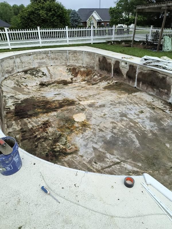 A dirty swimming pool with a white fence in the background.