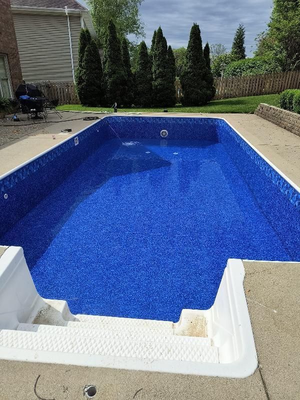A large swimming pool with a blue liner in a backyard.
