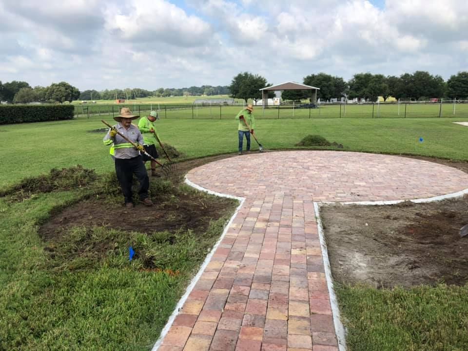 A group of people are working on a brick walkway in a park.