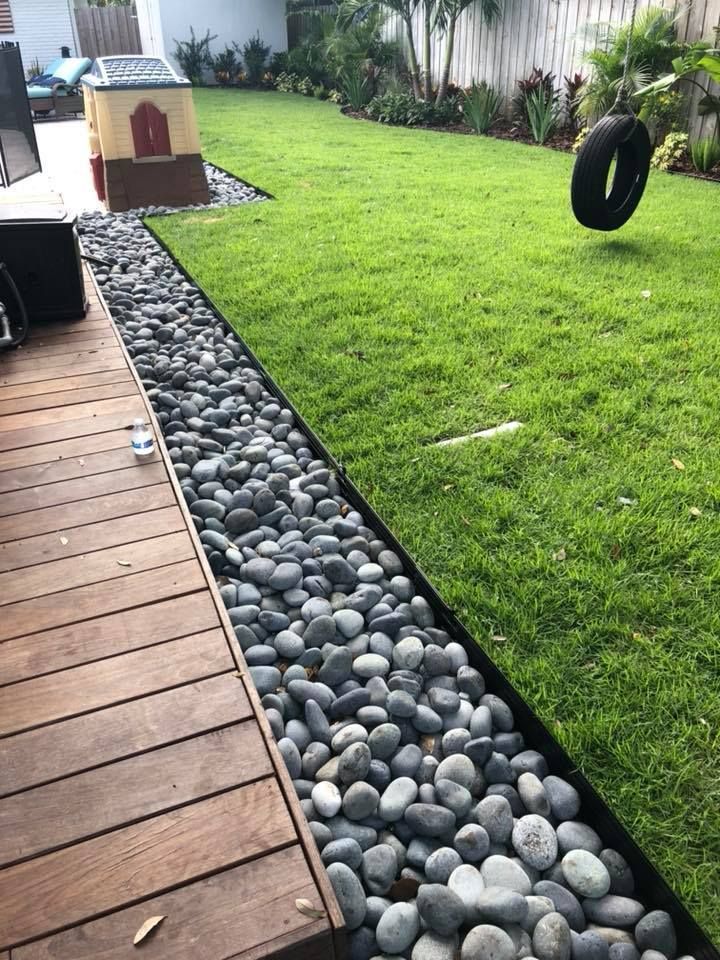 A tire swing is hanging over a lush green lawn next to a wooden deck.