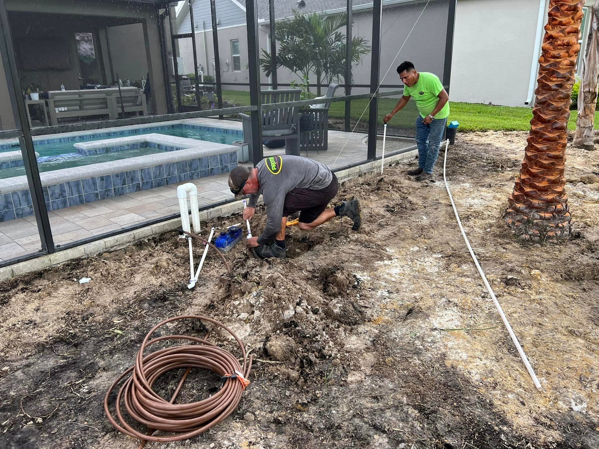 Two men are working on a sprinkler system in a backyard.