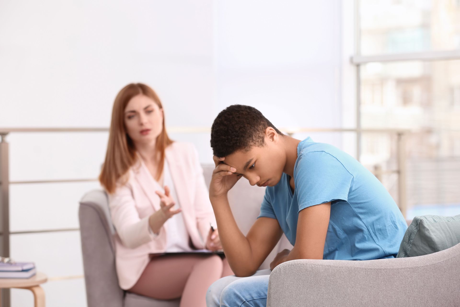 Person sits hunched on couch while counselor listens and takes notes in a bright office