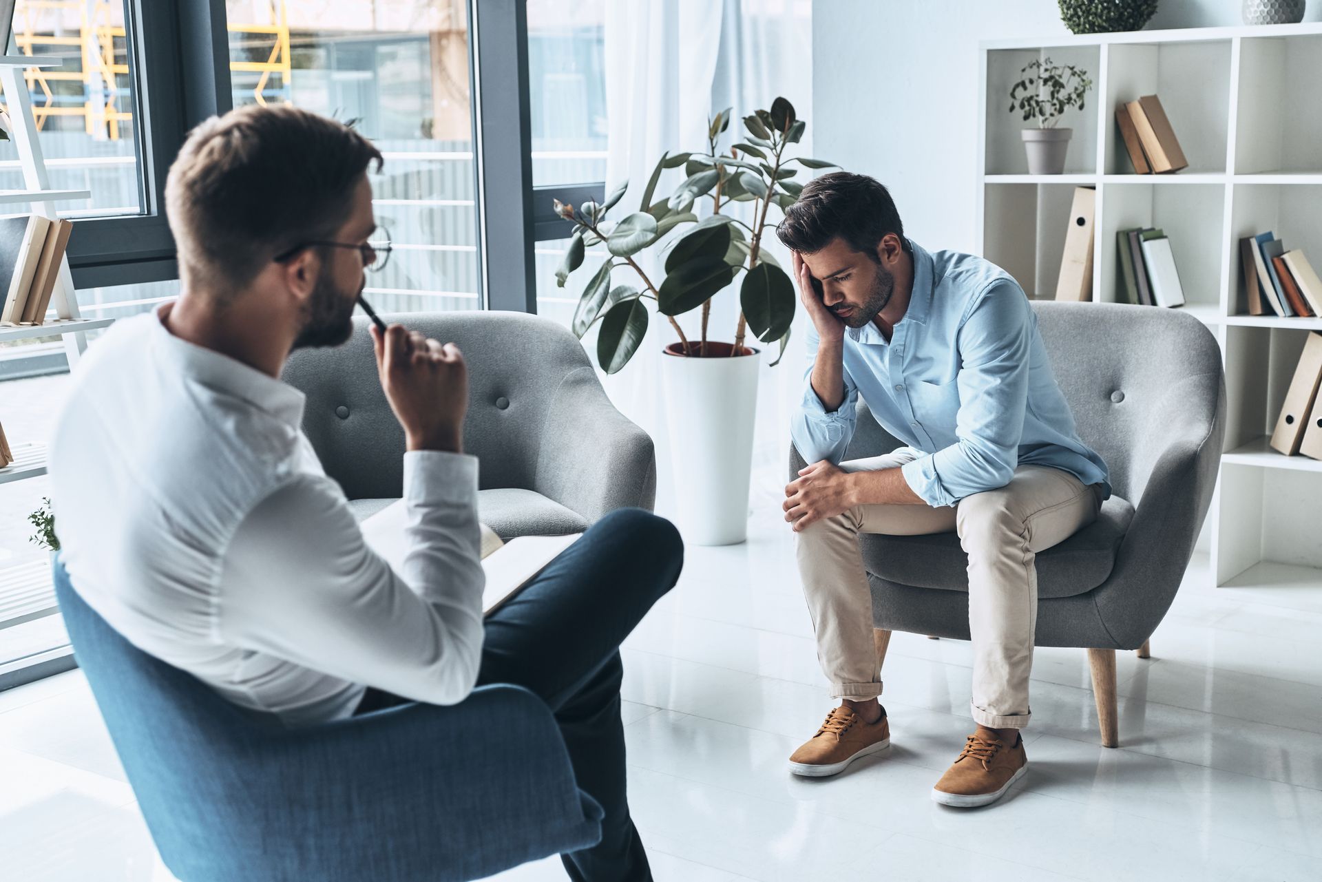 Two people sitting in armchairs, talking in a bright modern office lounge.