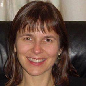 Smiling woman with brown hair seated on a black chair against a light curtain backdrop