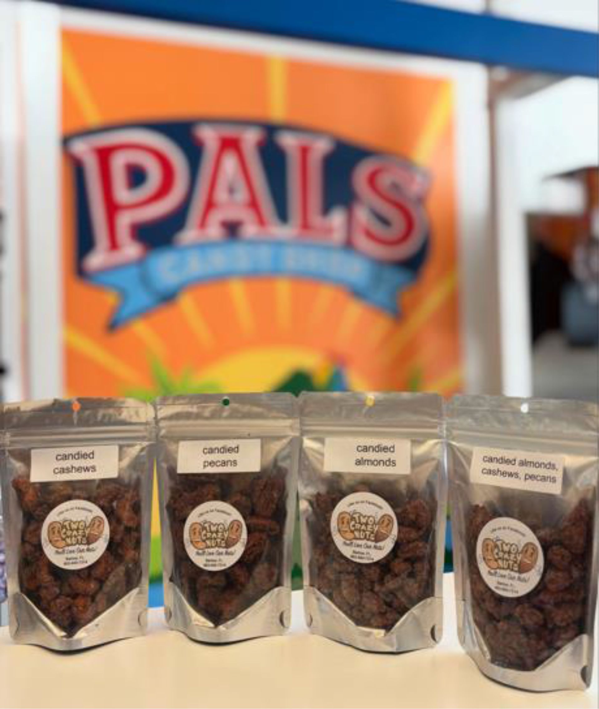 Four clear pouches of dried fruit in front of a Pals Candy Shop sign.