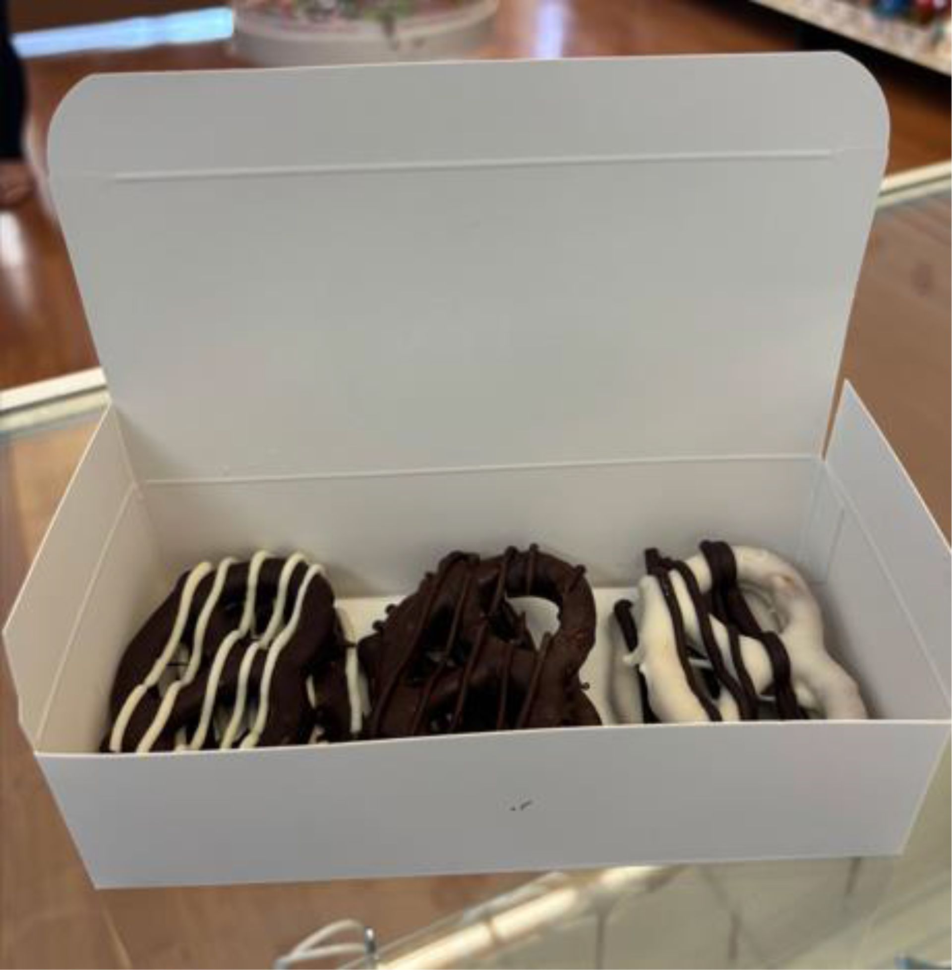 Three chocolate-covered pretzels in a white box, drizzled with white and dark chocolate.