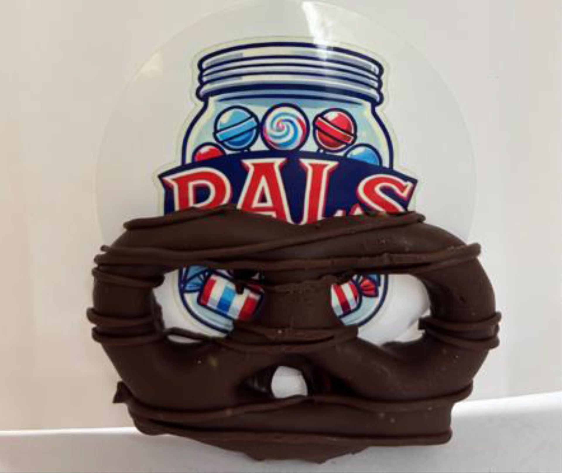Chocolate-covered pretzel with PALS logo; candy jar with blue, red, white candies, the word PALS in red text.