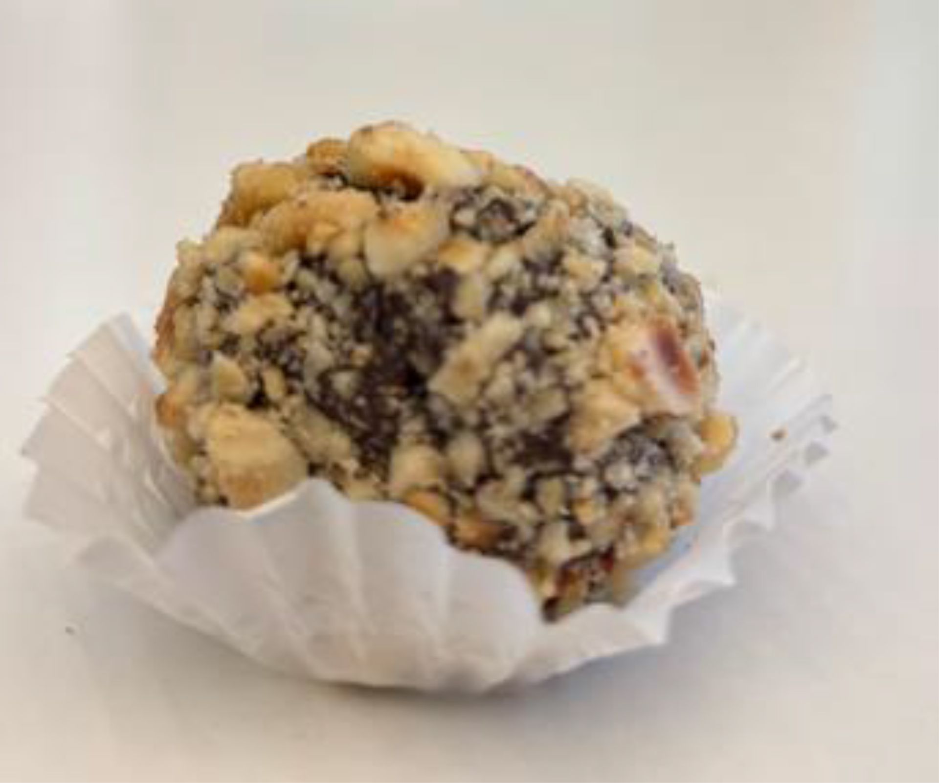 Chocolate truffle coated in chopped nuts, in a white paper cup.