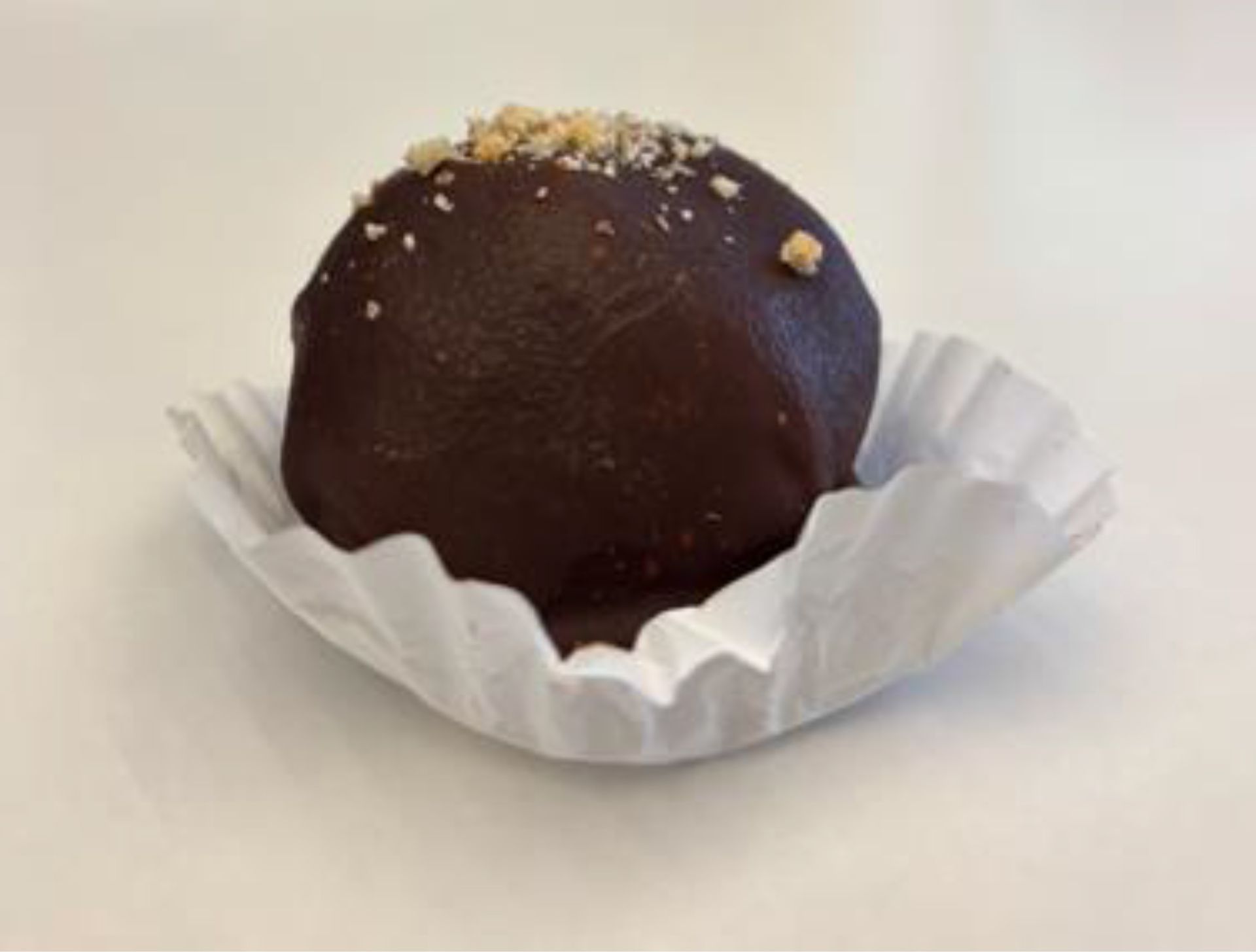 Chocolate truffle in a white paper cup, topped with chopped nuts.