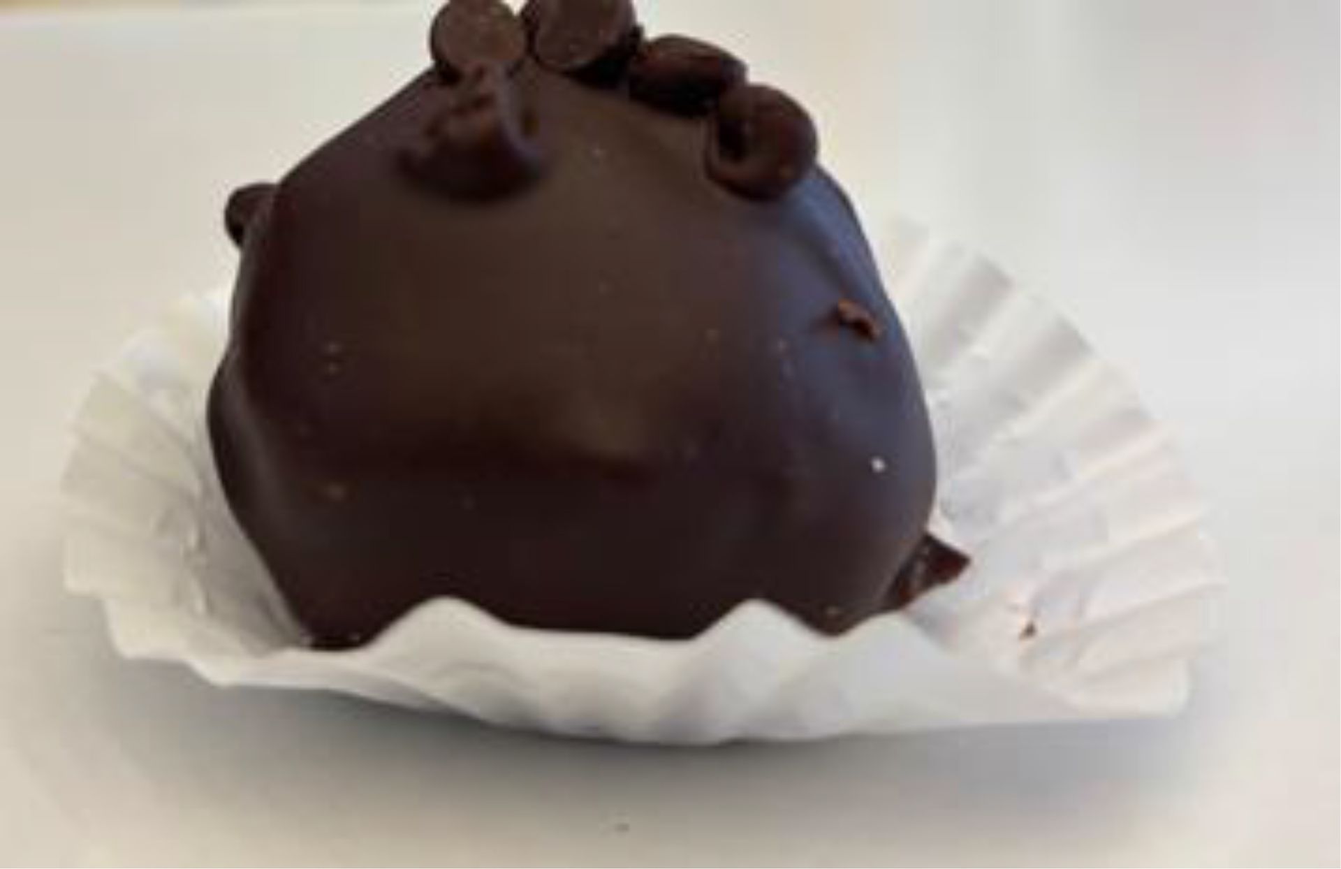 Chocolate-covered truffle with chocolate chips on top, in a white paper cup.