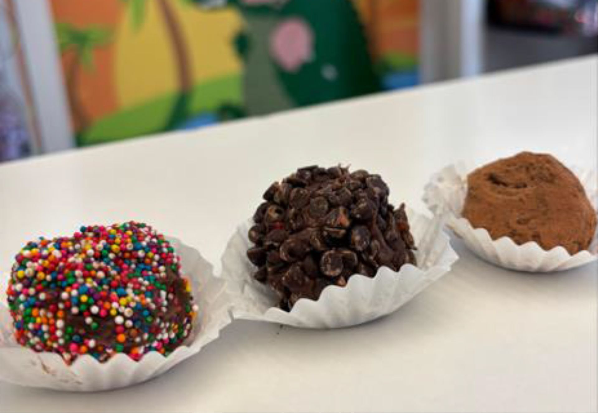 Three chocolate truffles in paper cups, covered in sprinkles, mini chips, and cocoa powder.