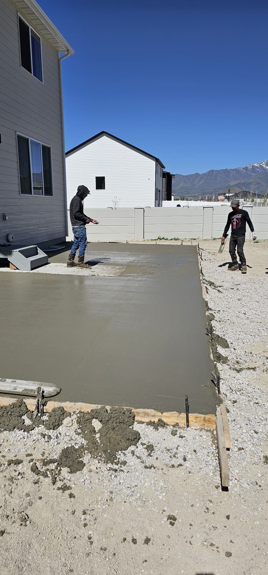 Two men are working on a concrete driveway in front of a house.