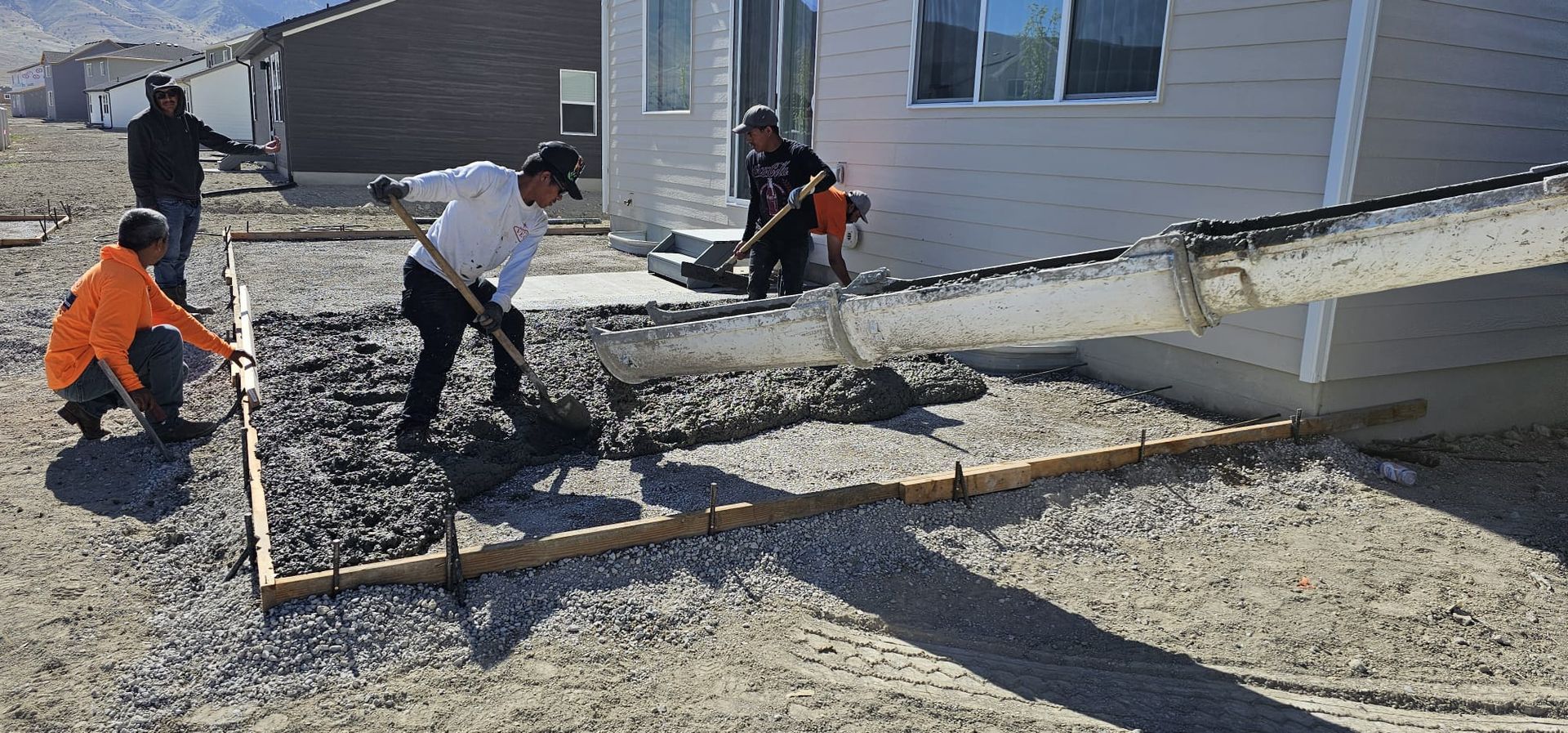 A group of construction workers are working on a concrete driveway in front of a house.