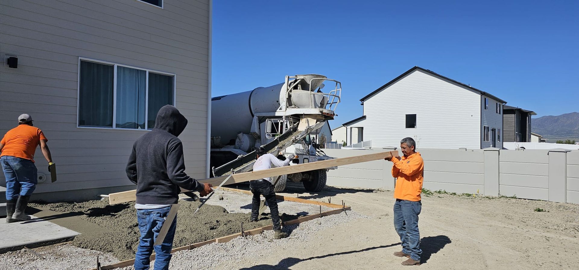A group of construction workers are working on a driveway in front of a house.
