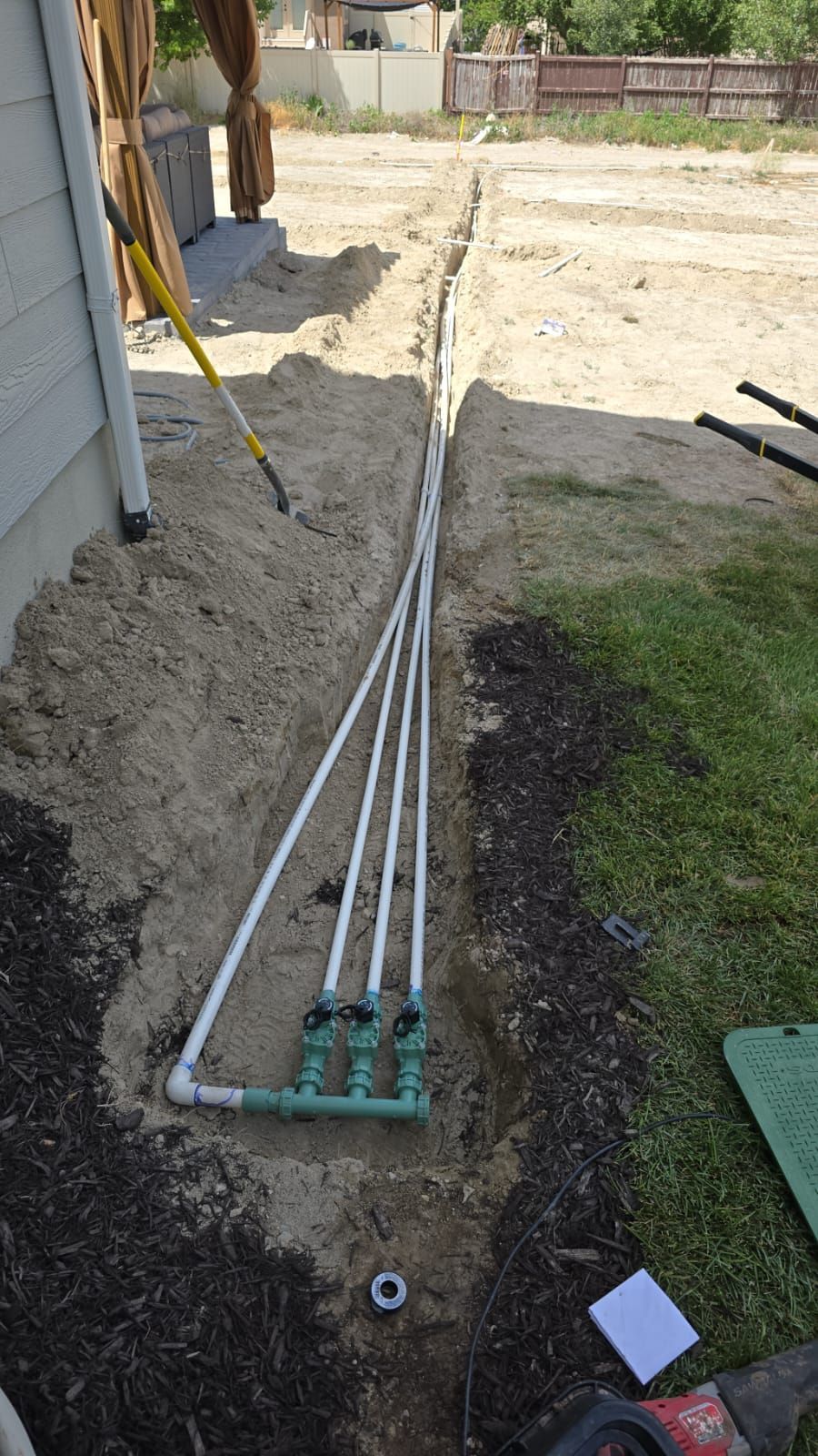 A bunch of pipes are laying in the dirt next to a house.