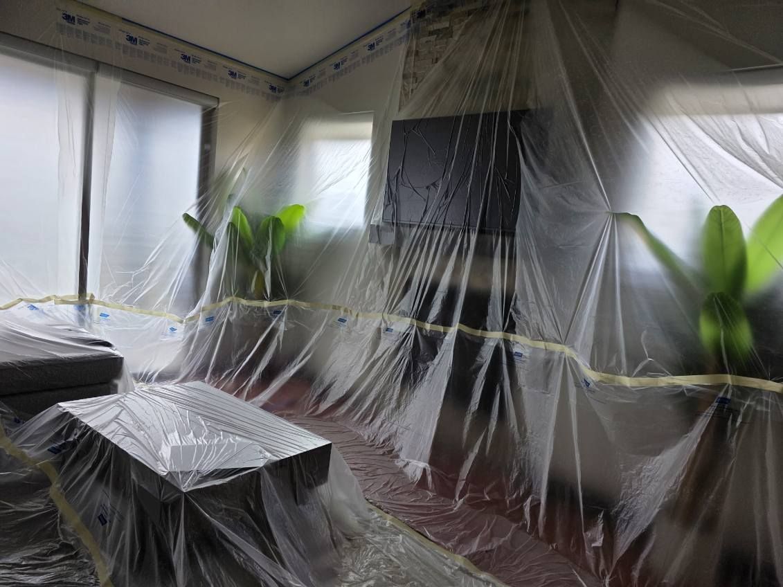 A living room is covered in plastic sheets.