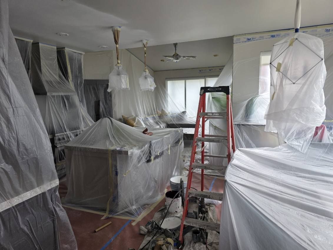A room with a ladder and a couch covered in plastic.