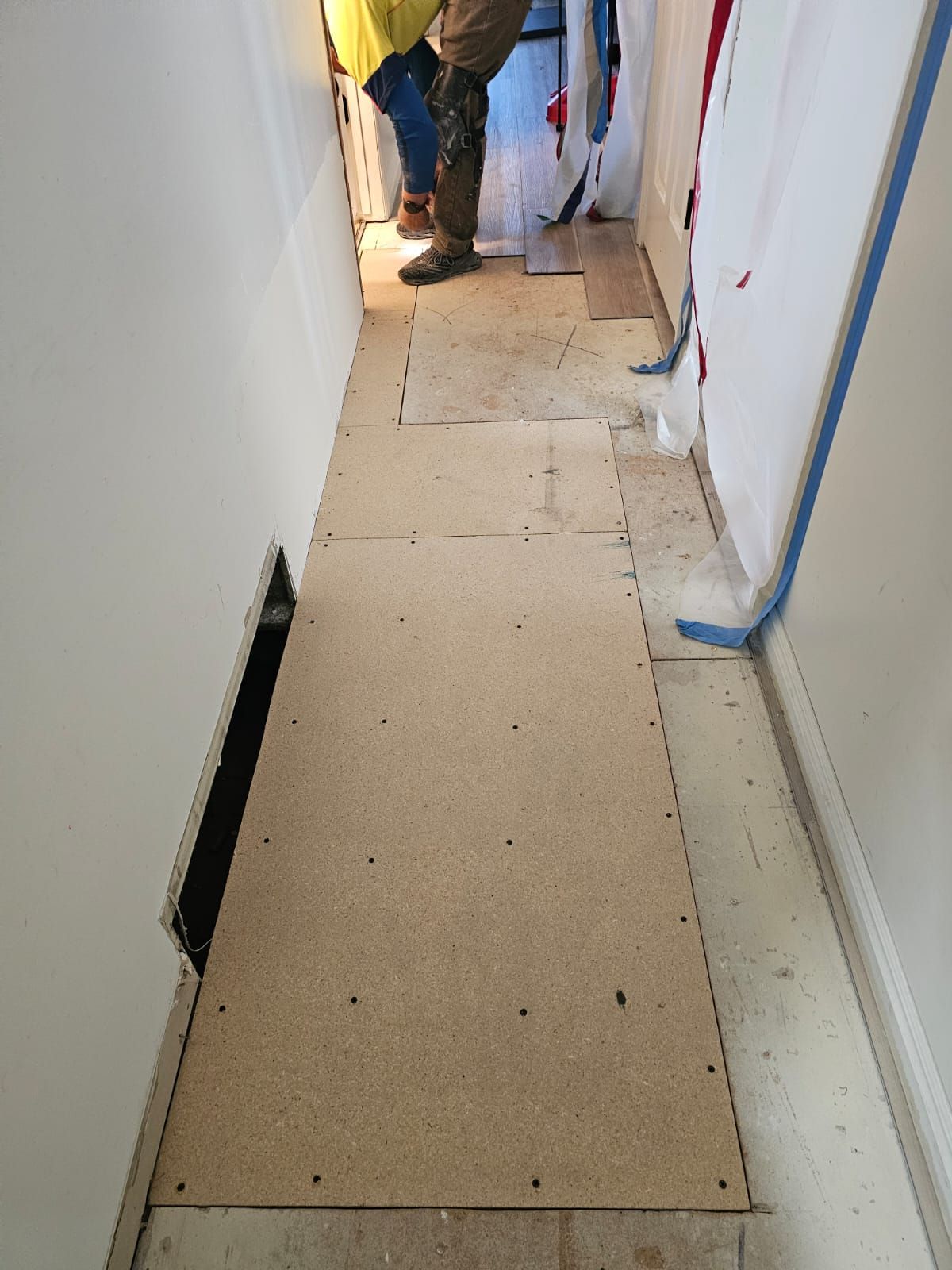 A person is standing on a wooden floor in a hallway.