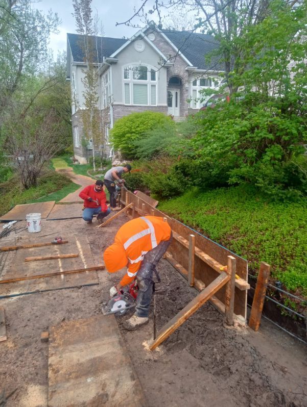 A group of construction workers are working on a sidewalk in front of a house.