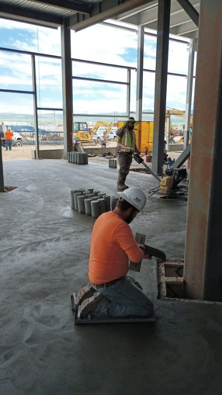 Two construction workers are working on a concrete floor in a building under construction.