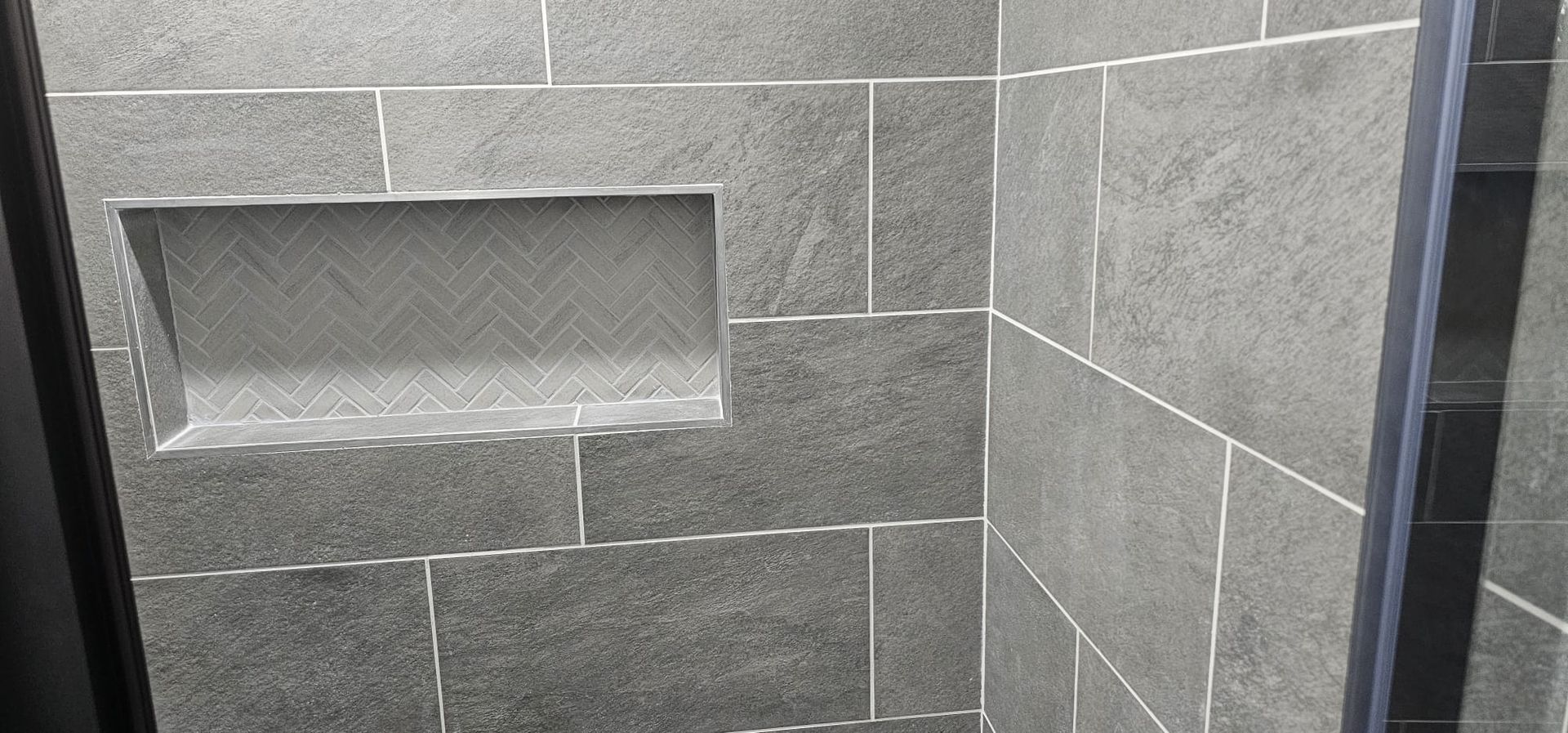 A shower stall with a shelf in the corner and a glass door.